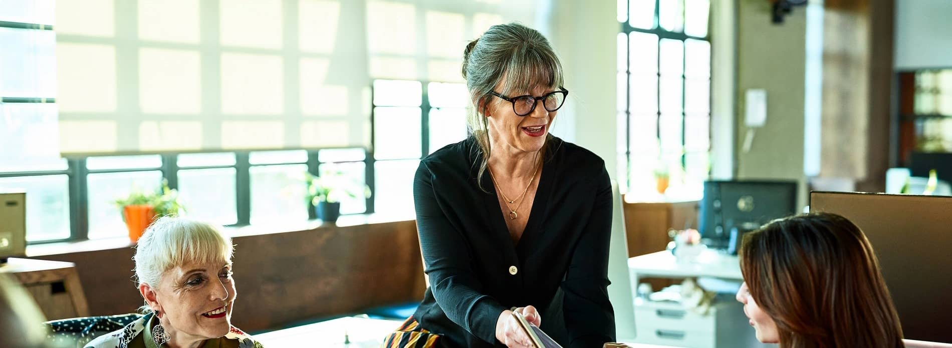 lady sitting on desk talking to colleagues 
