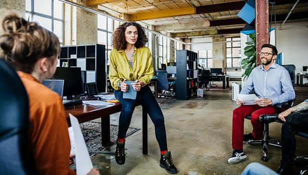 lady sitting on desk talking to colleagues 