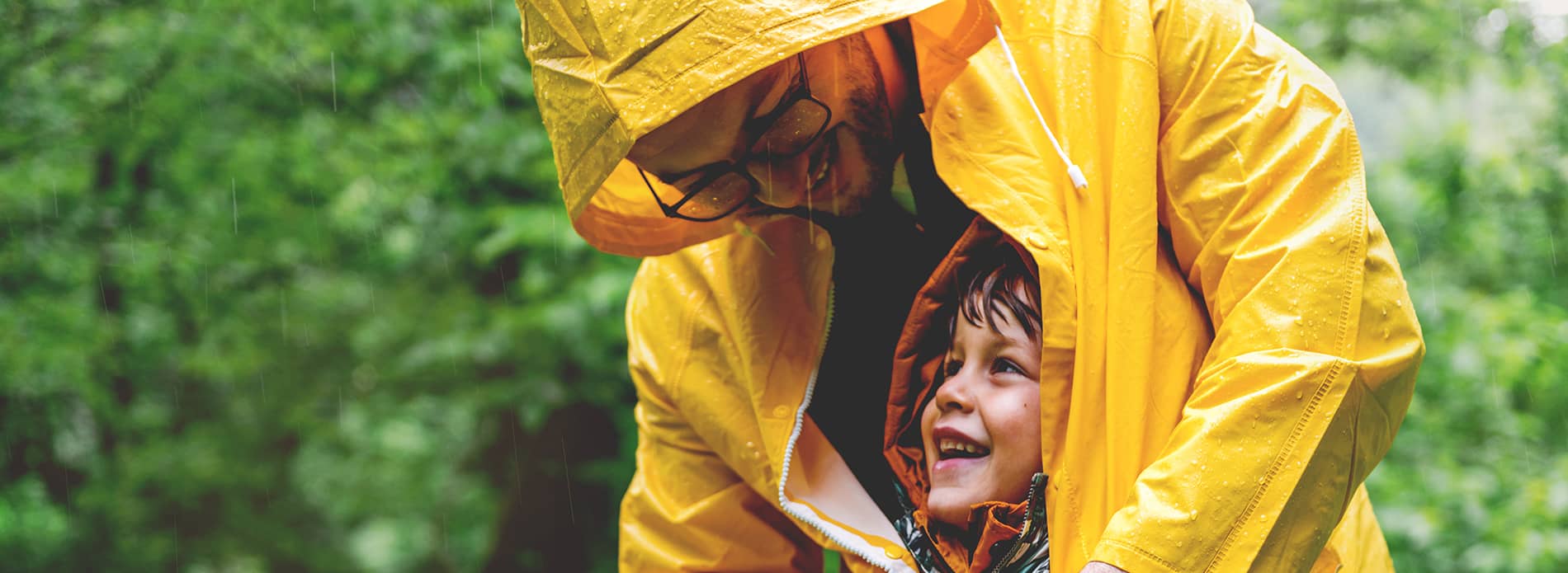 father shielding son with raincoat in the rain