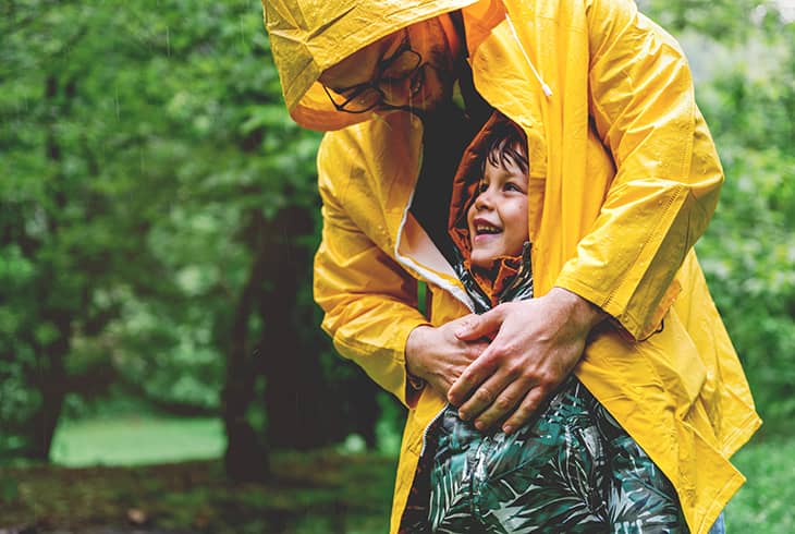 Father shielding son with raincoat in the rain