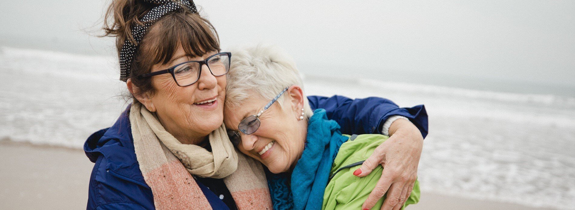 two elderly women hugging on the beach